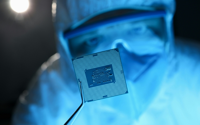半導体チップをピンセットで持って確認するクリーンウェア姿の作業員